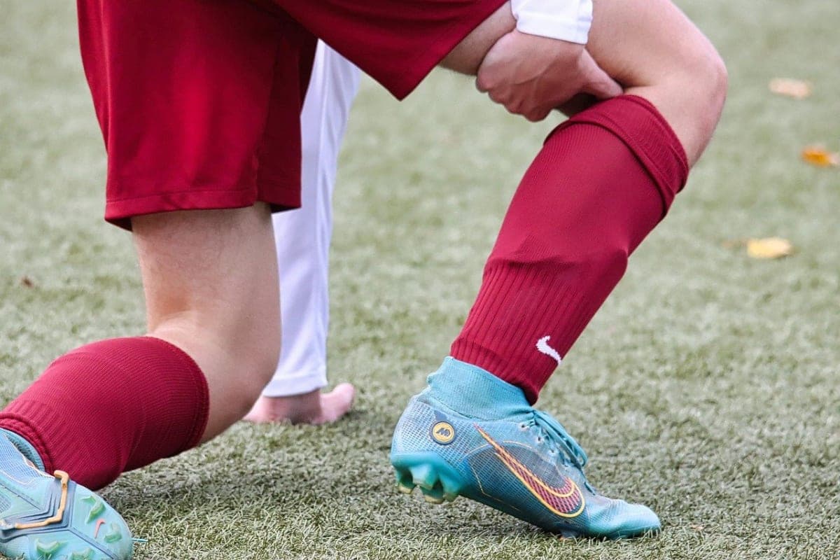 Futbol sahasında diz çökmüş oyuncunun eliyle dizini tutması